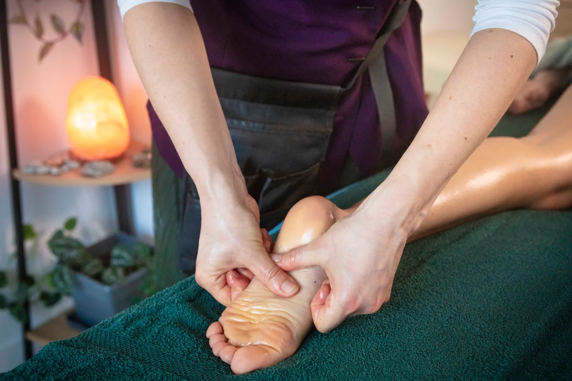 Massage du pied en réflexologie plantaire, lampe de sel en arrière-plan